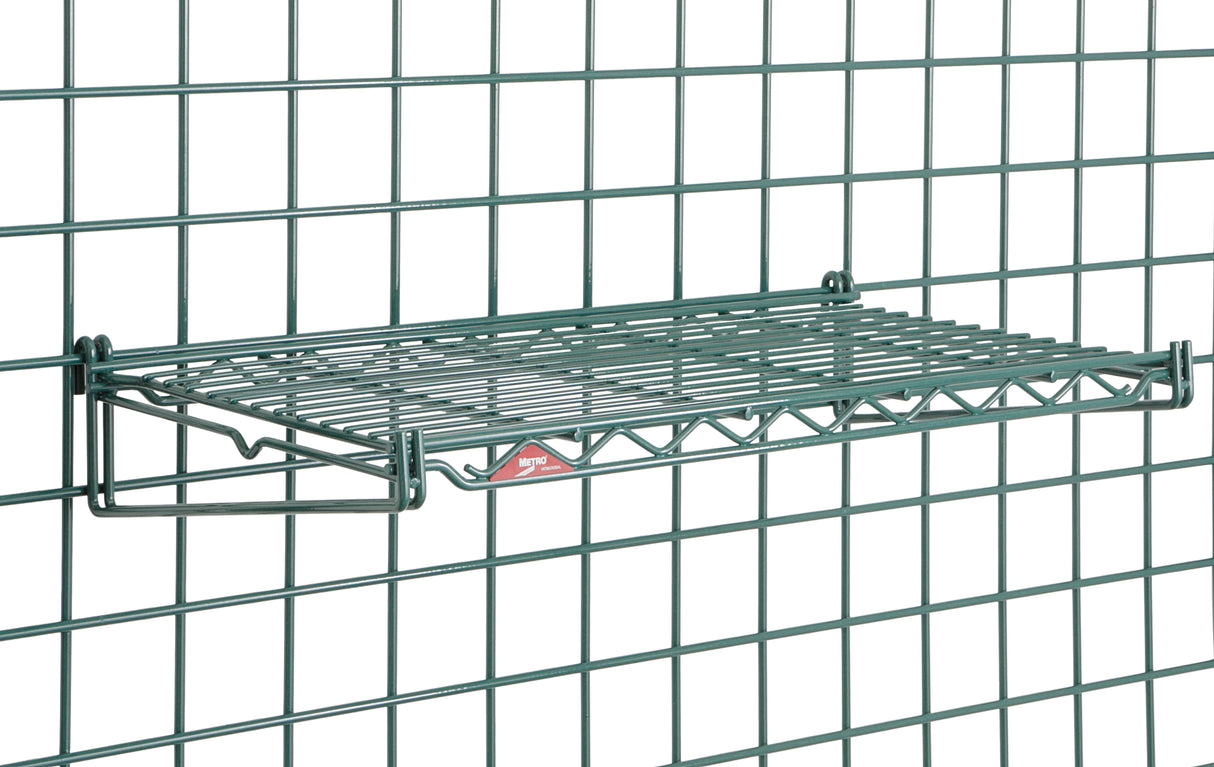 A Metroseal 3 green SmartWall Flat Grid Shelf is mounted on a matching green grid wall panel. The rectangular shelf features a metal lattice design with antimicrobial protection, held by two angled brackets and a small red and white label in front.