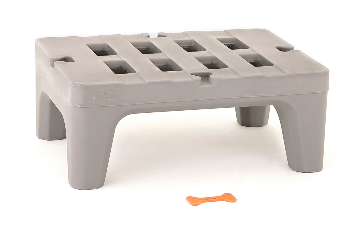 A gray plastic step stool made from corrosion proof polymer, with a slatted grid-like top and sturdy legs, stands on a white background. In front of the stool is a small orange bone-shaped object.