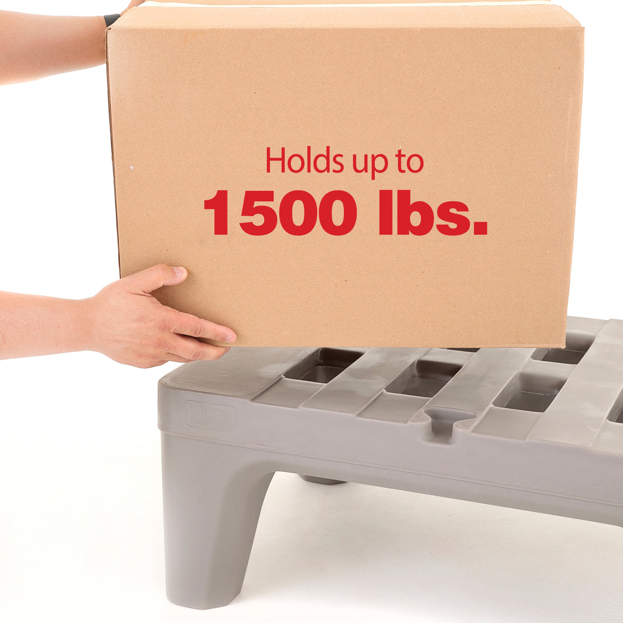 A person places a large brown box labeled Holds up to 1500 lbs. onto a gray dunnage rack with square slots. Only the person’s hands and arms are visible. The rack’s polymer construction stands out against the clean, white background.