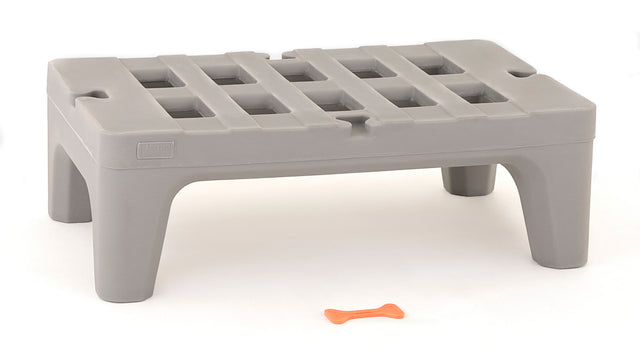 A small, gray, rectangular plastic step stool made from corrosion proof polymer with four wide legs and a slotted top sits on a white surface. In front of the stool, there is a small, orange, bone-shaped object.