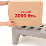 A person places a large cardboard box labeled “Holds up to 3000 lbs.” on a corrosion proof dunnage rack with four sturdy legs and slotted openings, against a plain white background.