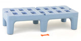 A light blue Dunnage Rack made from rust proof polymer with grid-like square openings sits on six short legs. In front of it, on a white surface, lies a small orange bone-shaped object. The overall setting is minimalist and brightly lit.