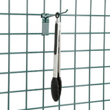 A pair of metal kitchen tongs with black silicone tips hangs from a SmartWall Prong Hook attached to a green wire grid panel. The grid has a rectangular pattern, and a small green clip is also attached above the tongs on the panel.