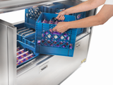A person puts a blue plastic container into a refrigerator with top-mount refrigeration.