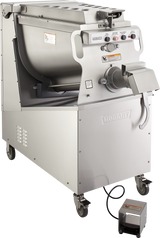 A large, industrial stainless steel Prime Mixer Grinder on wheels, featuring a tilt-back mixing bowl with 200 lb. capacity, push-button controls, a side chute, and foot pedal. The machine has vents and warning labels, set against a plain white background.