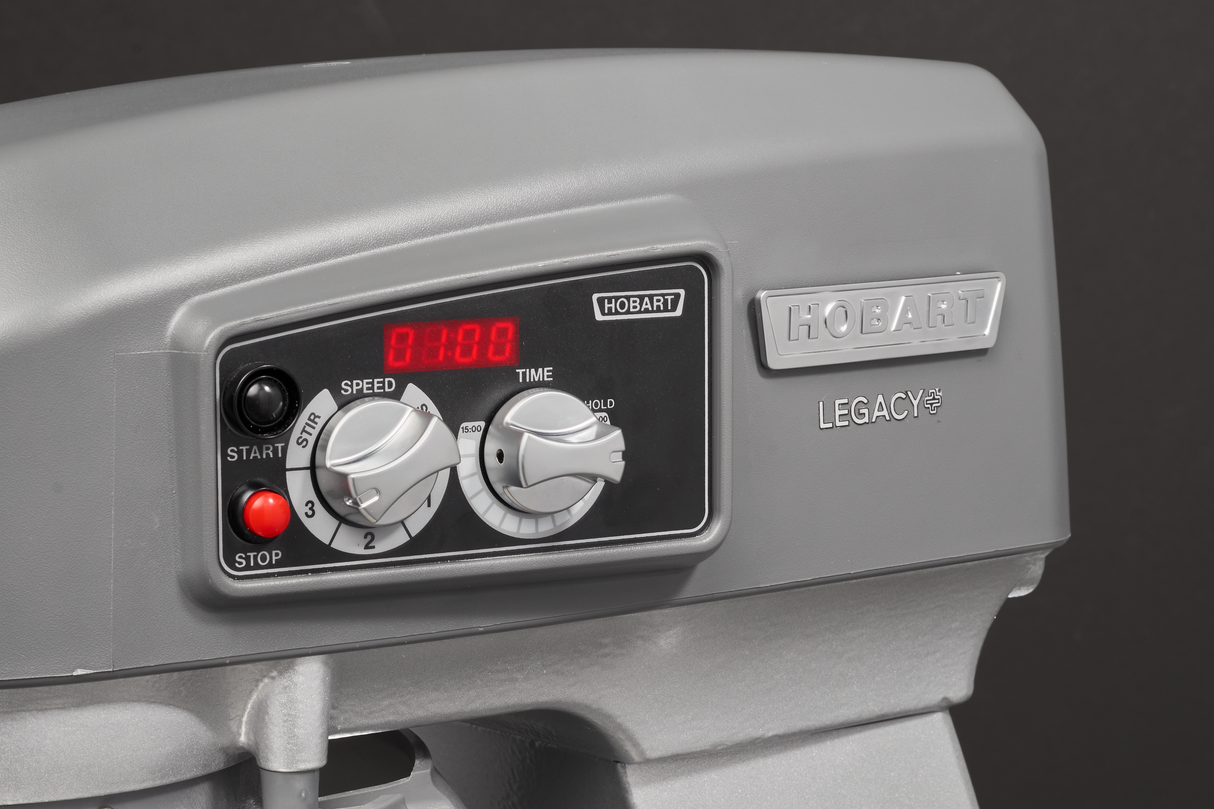 A close-up of a gray Hobart Legacy floor type mixer control panel. The panel features a red digital display, speed and time dials, and buttons labeled “Start,” “Stop,” and “Hobart.” The metal Hobart logo is prominently displayed on the right.