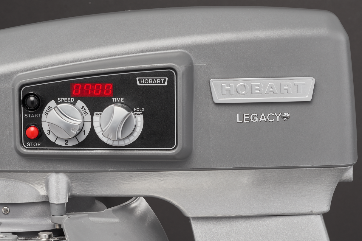 Close-up of the control panel on a gray Hobart Legacy planetary mixer. The digital red timer, knobs for “Speed” and “Time,” and start/stop buttons are visible. HOBART and LEGACY brand labels identify this robust floor mixer.