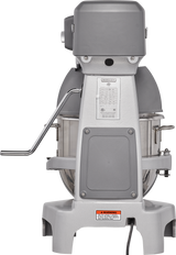 A commercial 20 quart planetary mixer with a metal bowl, gray body, and left-side control lever. The front displays a chart and warning label. This sturdy floor mixer stands on four legs, plugged in against a plain white background.