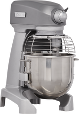 A large, industrial-grade gray planetary mixer with a stainless steel mixing bowl and protective metal wire guard. This Hobart 20 quart mixer features sturdy legs, a control knob on top, and prominent branding on the body and knob.
