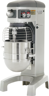 A large Hobart HL1400C correctional planetary mixer with a 140 quart stainless steel bowl and protective wire guard. The machine has control knobs, switches, and a digital display on a gray panel labeled Hobart Legacy, mounted on a sturdy metal base.