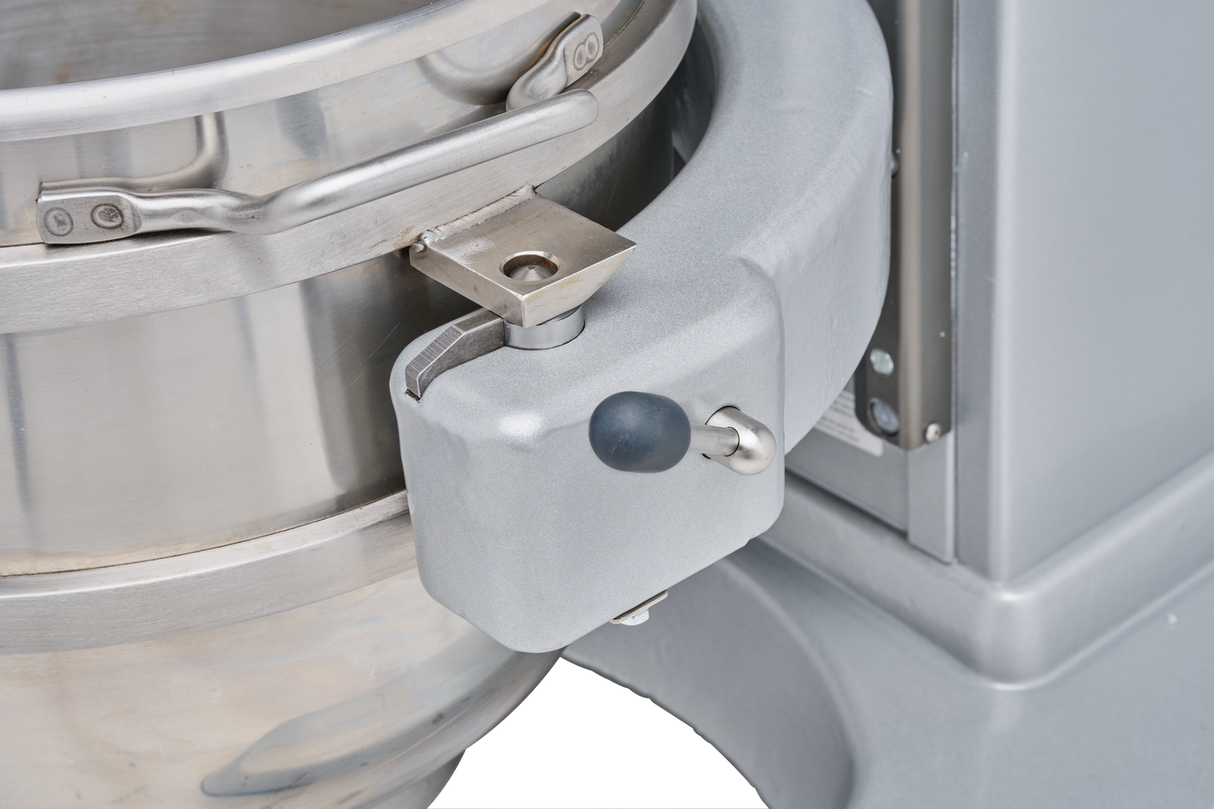 Close-up of a Legacy Planetary Mixer showing a large stainless steel mixing bowl secured with a metal latch and hinge mechanism. The mixer has a grey, sturdy frame with a black knob and lever for locking the bowl in place.