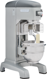 A large, silver Hobart Legacy Planetary Mixer with a metal mixing bowl, safety guard, and attached paddle beater. The 60 qt mixer features control buttons on the upper right, a sturdy base, and a rectangular block of butter inside the bowl.