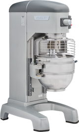 A large, industrial Hobart Legacy Planetary Mixer with a protective wire guard and 60 qt mixing bowl sits on a sturdy gray base. Controls and a red emergency stop button are visible on the top right corner.