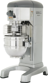 A large commercial dough mixer, the Hobart Legacy is a 60 quart planetary mixer made of stainless steel with a grey top. It features a protective wire guard over the mixing bowl and sturdy legs, ideal for heavy-duty use in commercial kitchens or bakeries.