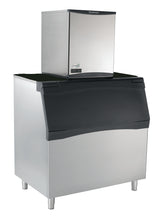 A commercial ice machine with a stainless steel exterior, featuring a large lower storage bin with a black, angled lid and a compact nugget ice maker on top, both branded “Scotsman.” The unit has short legs and a digital display on the ice maker.