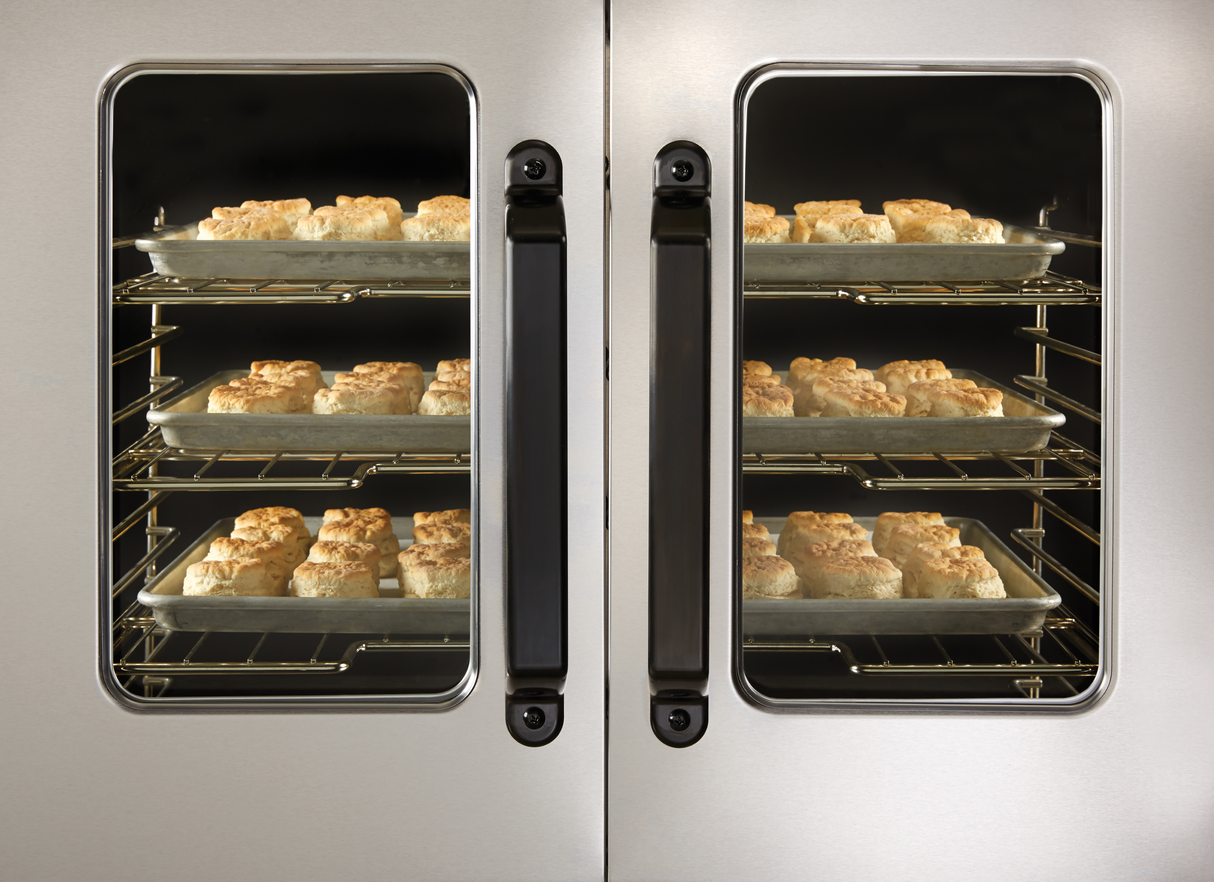 Rows of golden brown biscuits bake on metal trays inside a Vulcan VC5GD convection oven with double glass doors, revealing four racks filled with evenly spaced biscuits at various stages of baking.