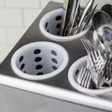 A close-up of a stainless steel cutlery holder with white, perforated polypropylene flatware cylinders. Some cups hold metal forks and utensils, while others are empty. The background shows a white tiled wall with a subtle grid pattern.