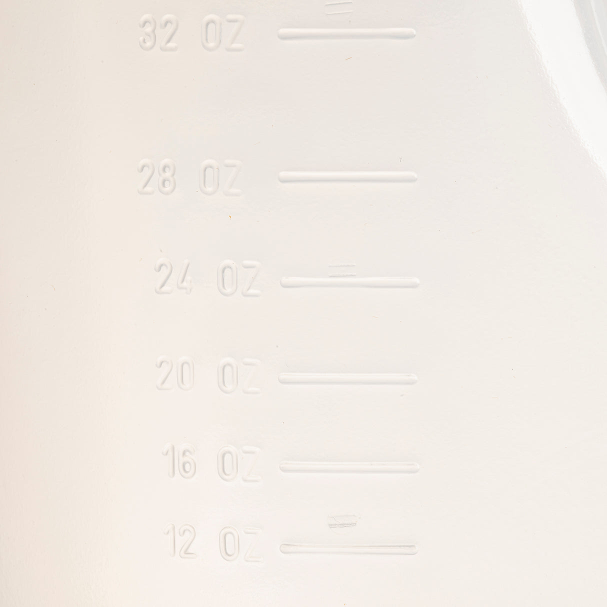 Close-up of a BPA free white plastic surface with embossed measurement markings in ounces, showing increments of 12, 16, 20, 24, 28, and 32 oz. The markings are aligned vertically on the left side.