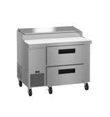A commercial Hoshizaki stainless steel pizza prep table featuring two drawers, a raised ingredient compartment with a metal lid, a white cutting board surface, ventilation grilles, control panel, and four caster wheels for mobility.