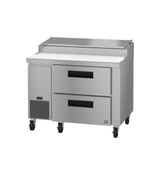 A Hoshizaki stainless steel pizza prep table features two horizontal drawers, a white cutting board surface, a hinged top, four caster wheels for mobility, plus a digital display and vent panel on the left front side.