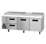 A commercial pizza prep table with a stainless steel finish features three doors, two refrigerated drawers, a flat worktop, four caster wheels, and a digital temperature control panel on the lower left side.