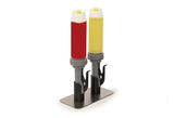 Two Nemco Food Equipment upright condiment dispensers sit on a shiny double Portion Pump Stand, one with red ketchup and the other with yellow mustard. Each has a gray pump, white cap, and is secured by black holders on the metal base.