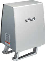 A stainless steel Hobart commercial dishwasher booster heater with a rectangular box shape, slanted front, and two metal supports at the bottom. The Hobart logo is on the front, alongside safety labels near the #12 hub for Power Drive Unit compatibility.