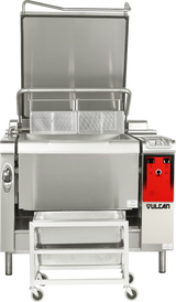 A large commercial tilting braising pan with an open lid, two mesh baskets inside, a bright red Vulcan control panel, and a stainless steel pan on a wheeled cart below the tilted skillet for catching contents—a true multifunction cooking unit.