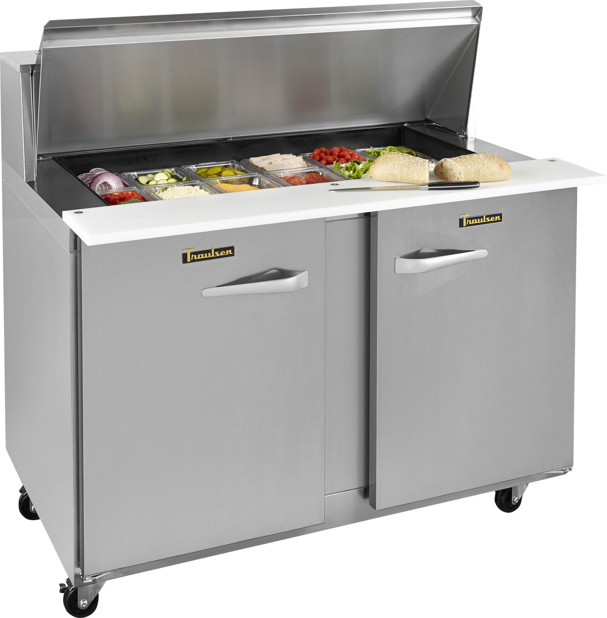 A Traulsen compact prep table refrigerator with a raised lid reveals compartments of sandwich ingredients like sliced veggies and meats. Two hoagie rolls rest on the white prep counter. The stainless steel unit features two doors and wheels for easy mobility.