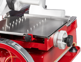 Close-up of a Berkel Fly Wheel Slicer shows a shiny metal platform with sharp spikes for holding food, a white adjustment dial with numbers, and various knobs. The chromium-plated carbon steel knife gleams against the black background.