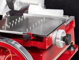 A close-up of a Berkel Fly Wheel Slicer shows a metallic tray with sharp spikes, a chromium-plated carbon steel knife, a numbered adjustment dial, and various mechanical details, all set against a dark background, highlighting its precision and industrial design.