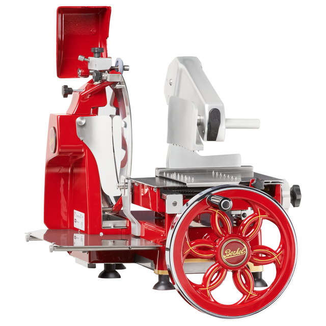 A vintage-style, red and silver Fly Wheel Slicer with a large hand-crank wheel labeled Berkel. It features a shiny chromium-plated carbon steel knife, black tray, and a classic retro industrial design with metal and plastic parts.