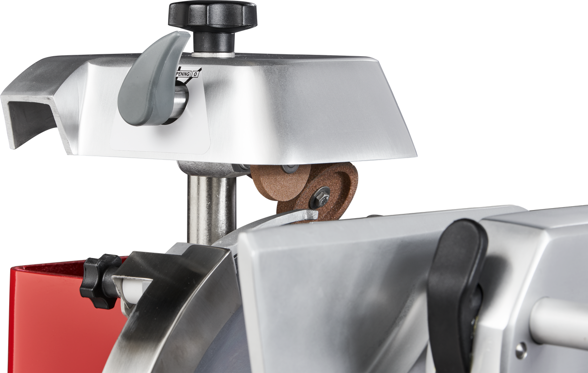 Close-up view of a commercial Berkel meat slicer, highlighting its built-in round sharpening stone above the chromium-plated carbon steel knife. The machine features metallic surfaces, black adjustment knobs, and a small area of red casing visible.