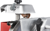 Close-up view of a commercial Berkel meat slicer, highlighting its built-in round sharpening stone above the chromium-plated carbon steel knife. The machine features metallic surfaces, black adjustment knobs, and a small area of red casing visible.