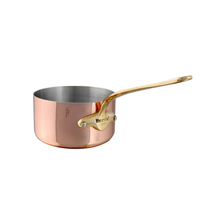A shiny copper saucepan, made in France, with a polished brass handle attached by two rivets. The interior is silver-colored stainless steel, and Mauviel 1830 is engraved on a small brass plate. The pan is set against a white background.