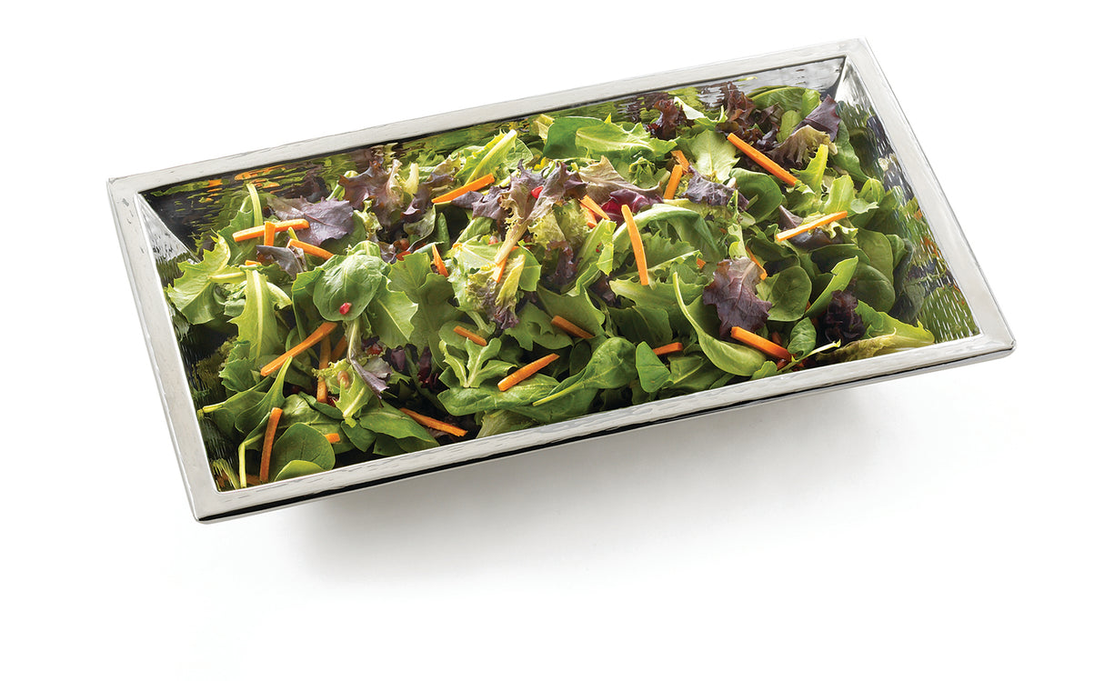 A rectangular stainless steel bowl filled with a mixed green salad, including leafy greens and thin orange carrot strips, set against a white background. Part of the Remington Collection Bowl series and conveniently dishwasher safe.