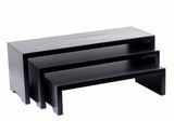 Three black rectangular Cascade Risers form a sleek nesting set, stacked together for a modern, minimalist look. Each TableCraft Products table features clean lines and a solid, blocky shape against a plain white background.