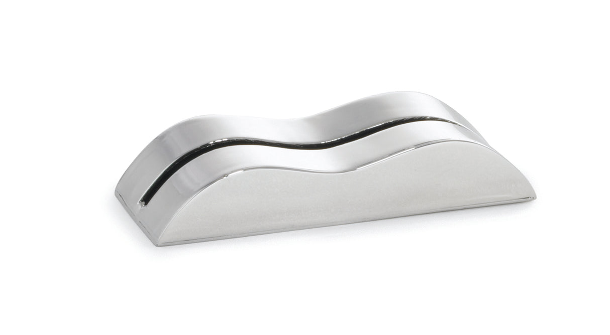 A sleek, metallic, wave-shaped card holder made of stainless steel with a reflective surface and a thin horizontal slot along its curved top, placed on a white background. The object has smooth edges and resembles a modern, minimalist desk accessory.