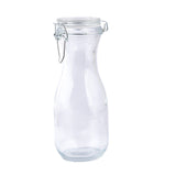 A clear glass carafe with a narrow neck and wide base, featuring a re-sealable hinged metal clasp and transparent lid, stands upright on a plain white background. The empty bottle reflects light, highlighting its smooth, clean surface.