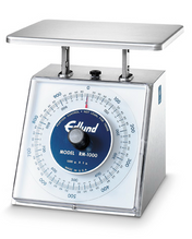 A stainless steel portion scale with a flat square top platform and a large round dial reading up to 1000 grams. The dial features black and blue markings, a black knob in the center, and Edlund MODEL RM-1000 printed on it. NSF certified.
