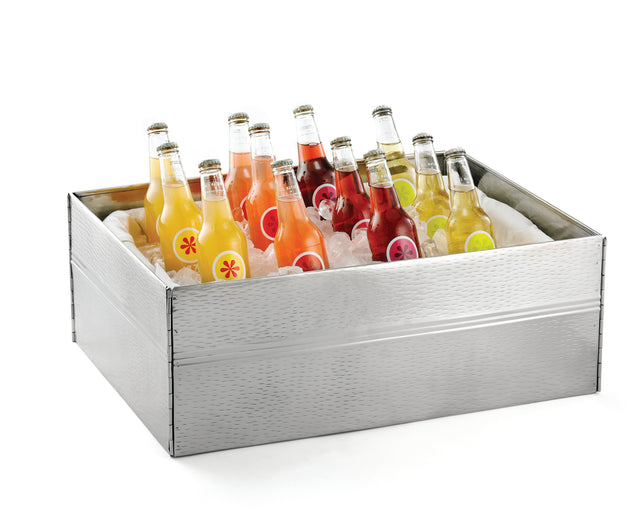 A silver Remington Collection Designer Tote Box with a stainless steel tote box frame holds twelve glass bottles of assorted colorful fruit sodas, each with vibrant fruit labels. The upright bottles are chilled on ice and the tote is dishwasher safe.