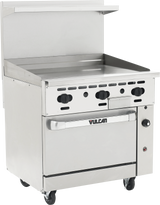 A commercial stainless steel restaurant range features four control knobs, a flat griddle top, and a spacious convection oven below with a Vulcan handle. It’s mounted on wheels with a raised backsplash and an upper shelf at the back.