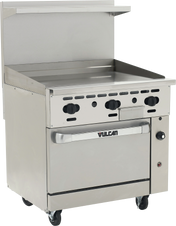A commercial stainless steel restaurant range with four black control knobs, a flat griddle top, a convection oven below labeled “Vulcan,” a backsplash with a small shelf, and four caster wheels for mobility. The range features a clean, industrial design.