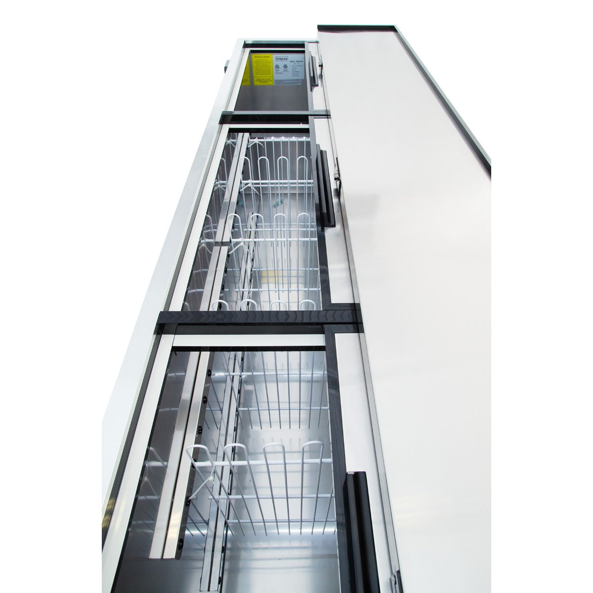 A tall Empura refrigeration commercial refrigerator is viewed from a low angle, showing empty metal wire shelves and transparent sliding glass doors. The clean interior features a white back panel, a yellow information label, and 29 cu. ft. capacity.