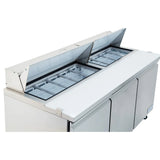 A stainless steel refrigerated sandwich prep table with two open hinged lids reveals multiple metal containers for storing ingredients. The white countertop provides a workspace, and three closed storage doors below complete this commercial refrigeration unit.