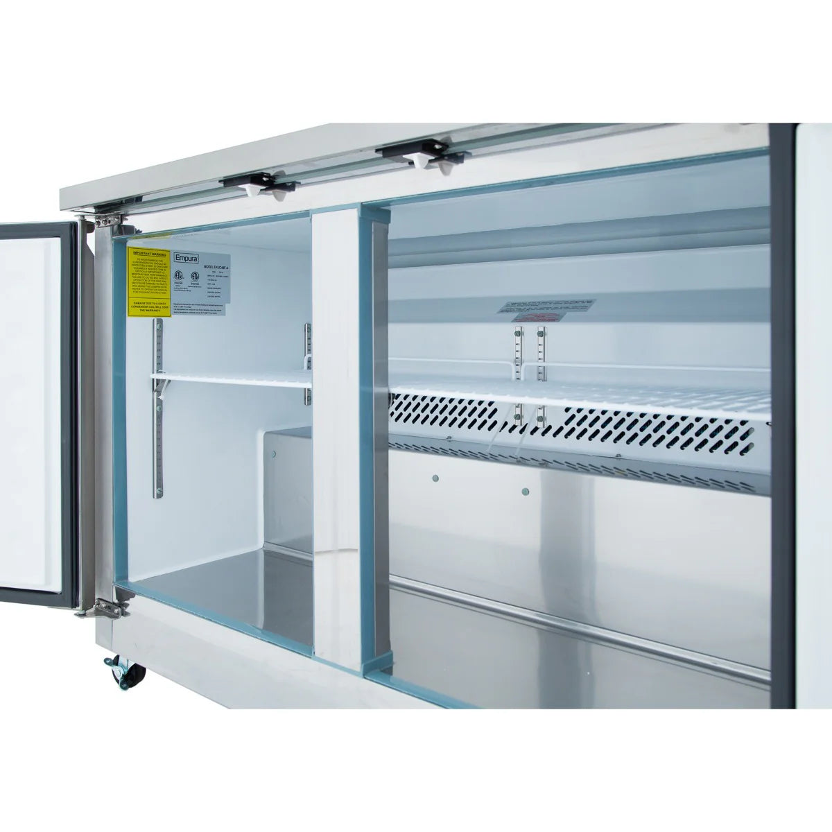 A close-up view of the inside of an Empura E-KUC48F Undercounter Reach-In Freezer with the door open, showing a clean, spacious interior with metal shelving supports, ventilation grates at the back, and a safety label on the inside wall.