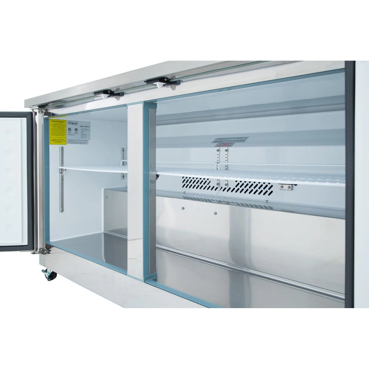 A close-up view of the inside of a commercial refrigerator by Empura Refrigeration shows open sliding glass doors, metal shelves, and a spotless interior with ventilation grilles and LED lighting. The left door of this Undercounter Reach-In Refrigerator is partially open.