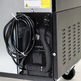 Close-up of the lower side of an Empura Refrigeration unit with mesh covering the components inside. A coiled black power cable hangs on a hook. The machine is on wheels, and a yellow caution label sits above the mesh—typical for back bar coolers.