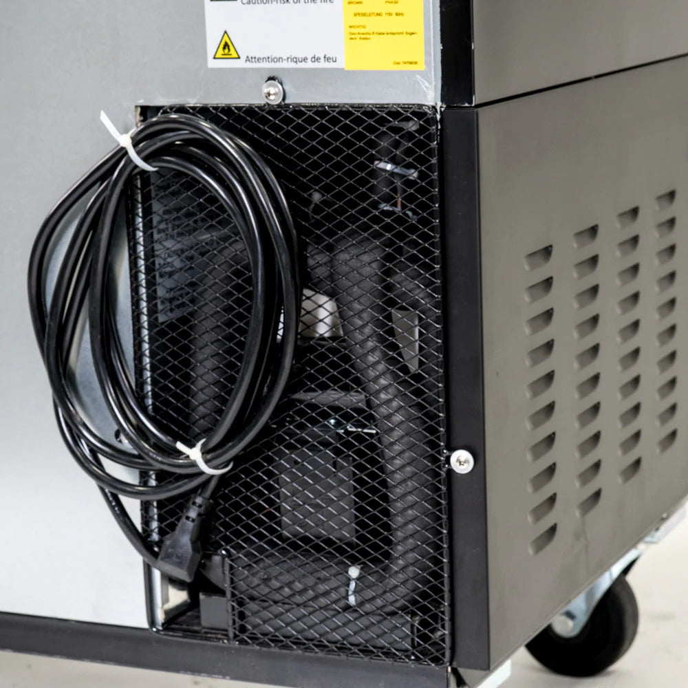 A close-up of the lower side of a black Empura Refrigeration machine shows a coiled power cord, vented metal panels, and internal components visible through a mesh cover. A yellow warning label about fire risk is attached near the top.