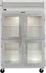 A large Traulsen commercial stainless steel reach-in refrigerator with four glass doors, metal handles, and visible wire shelves inside. The unit includes wheels, top ventilation, and a digital temperature display on the upper left.